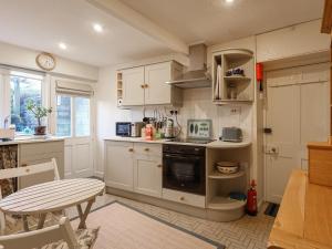 cocina con armarios blancos, mesa y fogones en September Cottage, en Lechlade