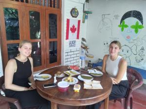two women sitting at a wooden table with food on it at Sigiriya Lions Rest Hostel in Sigiriya