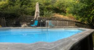 an empty swimming pool with an umbrella and chairs at Gîte du BONELLI in Malarce-sur-la-Thines