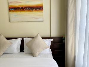 un letto con cuscini bianchi e un dipinto sul muro di Apartment in Nairobi West a Nairobi