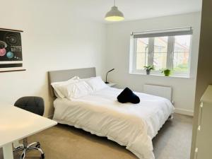 ein Schlafzimmer mit einem weißen Bett mit einer schwarzen Katze drauf in der Unterkunft Stunning Modern Four Bed Home Near Witney & Oxford in Oxford