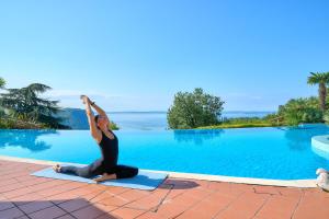 Eine Frau macht Yoga neben einem Schwimmbecken in der Unterkunft Madrigale Panoramic Lifestyle & Soulful Hotel in Costermano sul Garda