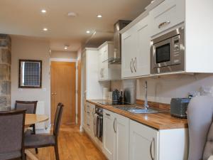 uma cozinha com armários brancos, uma mesa e um micro-ondas em Roslin Chapel Cottage - Uk49193 em Roslin