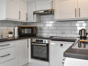 eine Küche mit weißen Schränken und einer Mikrowelle in der Unterkunft Crooklets Cottage in Bude