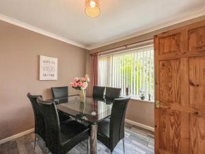 a dining room with a glass table and black chairs at Little Orme Cottage in Penrhyn Bay