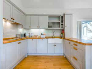 a white kitchen with white cabinets and wooden floors at Lavender Barn in Heacham +17 photos