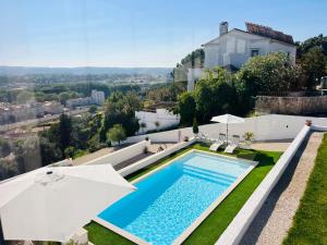 a swimming pool with an umbrella and a house at Vila Pombal Tomar Apartments - Pool & City Views in Tomar