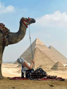 Una mujer sentada junto a un camello frente a las pirámides. en Desert Glow Pyramids INN, en El Cairo