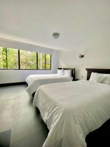 two beds in a white room with windows at Latín Boutique in Bogotá