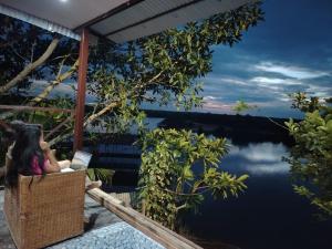 a woman sitting in a chair with a laptop overlooking a lake at El Bullicio de la Cabaña in Iquitos
