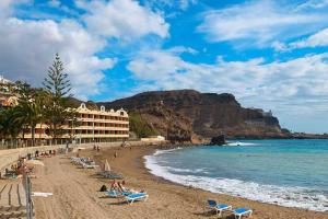a beach with chaise lounges and a hotel and the ocean at Mogán Vista Bonita in Mogán