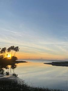 a sunset over a body of water with palm trees at Pousada Plenamar in Maragogi
