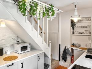 a kitchen with white cabinets and a staircase with a microwave at Wisteria Cottage in Harrogate