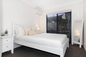 a white bedroom with a white bed and a window at The Enclave - A Family Alfresco Retreat in Dunsborough