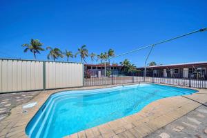 a swimming pool in a yard with a fence and palm trees at Pearly Shell Motel in Bowen