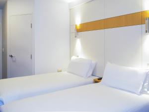 two beds in a hotel room with white sheets at ibis Budget - Gosford in Gosford