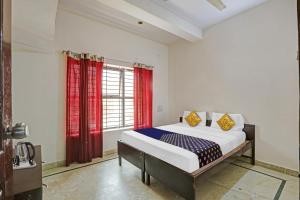 a bedroom with a bed and a window with red curtains at Hotel O Vishu Moni Residency in Mysore