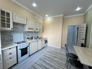 une cuisine avec des armoires blanches et une table avec des chaises dans l'établissement Уютная 1 комнатная квартира в ЖК БАВАРИЯ, à Aqtöbe