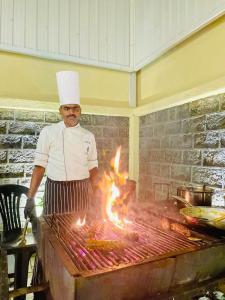 un homme portant un chapeau de chef cuisinant sur un gril dans l'établissement Collingwood Queen - Boutique Hotel, à Nuwara Eliya