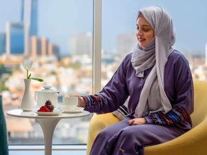 a woman sitting in a chair with a cup of coffee at Adagio Aparthotel Jeddah Malik Road in Jeddah