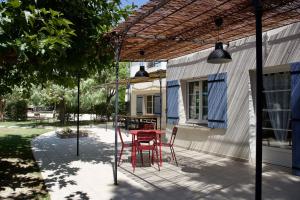 un patio con una mesa roja y sillas bajo una pérgola en Mas de Cerier, en Saint-Gilles