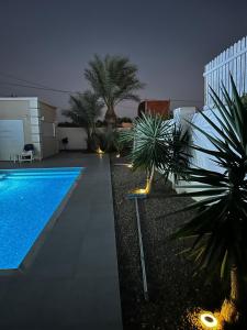 a backyard with a swimming pool and palm trees at night at Villa Maghrebi in Al Ḩaddādah