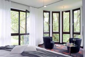 a bedroom with windows and a bed and two chairs at Mintrops Land Hotel Burgaltendorf in Essen