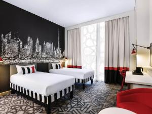 a hotel room with two beds and a red chair at ibis Styles Dubai Airport Hotel in Dubai +32 photos