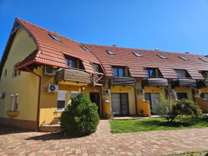 a yellow building with a red roof and windows at Lagom Apartman in Gyula