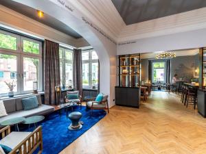 a living room with a couch and tables and windows at Mercure Hotel Luebeck City Center in Lübeck