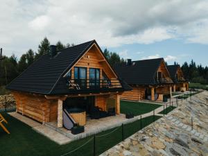 a log home with a black roof at Domki Osada Klenina SAUNA & BALIA in Kamienica