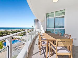 a balcony with a wooden table and chairs and the beach at Stylish 3 Bedroom Apartment with Pool, Sauna & Gym in Gold Coast