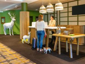 deux femmes debout à un comptoir dans un bureau avec des animaux dans l'établissement Ibis Styles Arlon Porte du Luxembourg, à Arlon