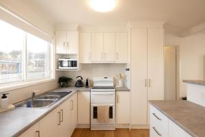 Una cocina blanca con fregadero y estufa. en Seafoam Beach Retreat, en Surf Beach 10 fotos más