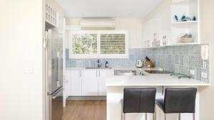 a white kitchen with white cabinets and black chairs at The Poplars Apartment Nelson Bay with Swimming Pool in Nelson Bay
