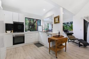 a kitchen with white cabinets and a table and a chair at Shellies Twin Beach Houses in Sawtell