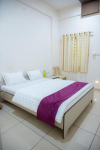 a white bedroom with a large bed with a purple blanket at hotel seven beach inn in Mandvi