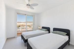 two beds in a white room with a window at Bahía Mar Apartamento in Puerto de Mazarrón