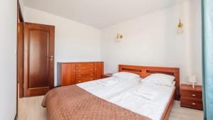 una camera da letto con letto, lenzuola bianche e mobili in legno di Flatbook Apartamenty - Krynica Morska Margo a Krynica Morska