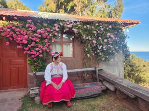 a woman sitting in front of a house with flowers at Casa de Alejandra llachon in Llachon