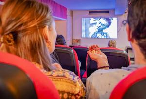 a woman sitting in a seat watching a man on a screen at Will & Tate City Stay in The Hague