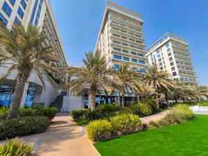 two tall buildings with palm trees in a park at Modern 1BR with Beach and Pool in Al Marjan Island in Ras al Khaimah