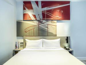 een slaapkamer met een wit bed en een schilderij bij ibis Bangkok IMPACT in Nonthaburi