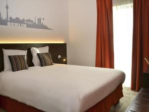 a bedroom with a large white bed with orange curtains at Ibis Styles La Louvière in La Louvière