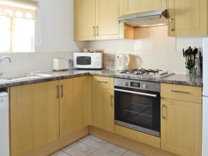 a kitchen with wooden cabinets and a stove and a microwave at Nightingale Cottage- 25115 in Flamborough