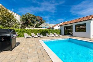 a swimming pool with chairs and a grill next to a house at Modern Villa Christian with pool, sauna, and jacuzzi, 10 min walk from the beach in Malinska