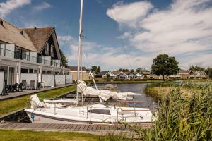 a white boat docked in a river next to a house at Herenhuizen 6 of 8 persoons geschakeld - Boutique Parc Pharshoeke in Heeg
