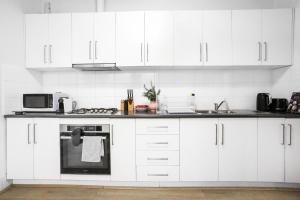 a white kitchen with white cabinets and a microwave at Pyrmont NSW - 3 Bedroom Apartment- 8 Guests - NetFlix in Sydney
