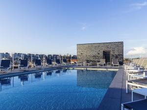 a swimming pool with chairs and a building in the background at Mercure Blankenberge in Blankenberge
