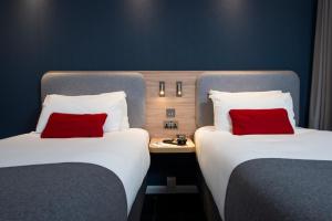 two beds with red pillows in a hotel room at Holiday Inn Express London - Dartford by IHG in Dartford